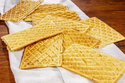 Un mucchio di croccanti ferratelle abruzzesi, dolci tradizionali dorati, disposte su un panno bianco su un tavolo di legno.