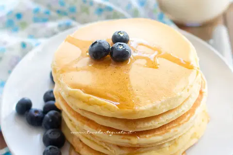 Pancakes senza glutine dorati, impilati e guarniti con mirtilli freschi e sciroppo d'acero.