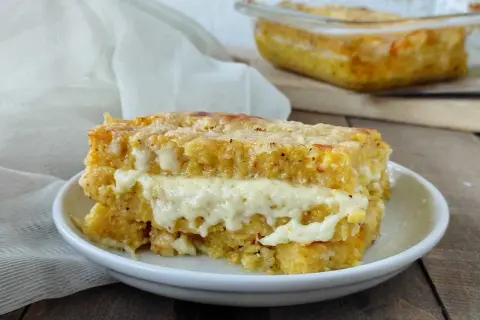 Una fetta di pasticcio di polenta con formaggio filante, cotto al forno e servito su un piatto bianco.