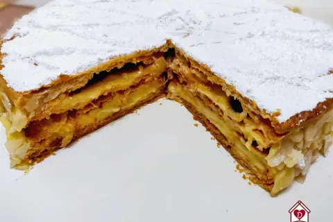 Una fetta di torta millefoglie con crema pasticcera e mandorle, cosparsa di zucchero a velo.