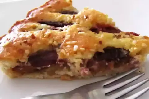 Una fetta di torta con prugne fresche, con crosta dorata e ripieno succoso, pronta per essere gustata.