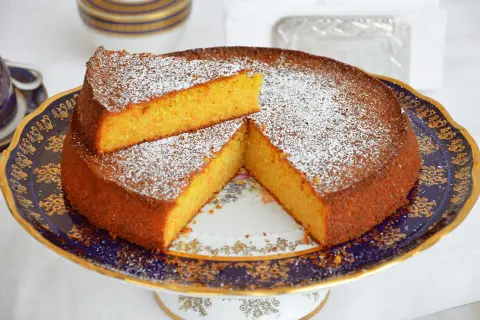 Una deliziosa torta carote e mandorle, spolverata di zucchero a velo, servita su un elegante piatto blu e oro.