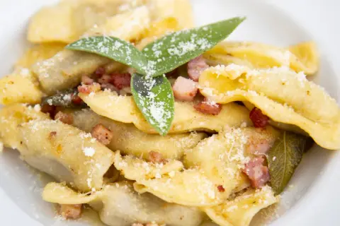 Un piatto di casoncelli alla bergamasca, ripieni e conditi con burro, salvia e pancetta croccante, spolverati di parmigiano.