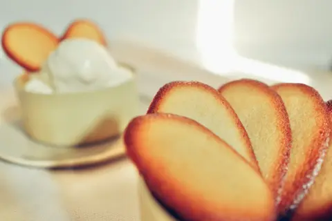Biscotti croccanti a forma di lingue di gatto, alcuni in primo piano, altri decorano una coppa di panna montata.