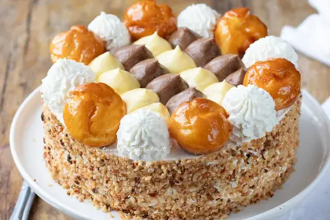 Una magnifica torta Saint Honoré, decorata con bignè caramellati, ciuffi di panna montata e crema pasticcera al cioccolato e vaniglia.