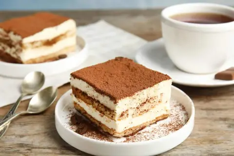 Delizioso tiramisù, perfetto per la tua tiramisù ricetta benedetta. Servito su un piatto bianco con caffè e cucchiaini.