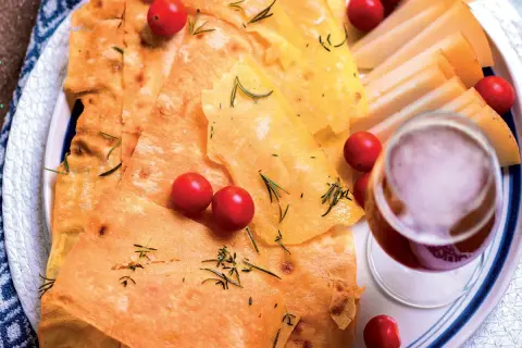 Pane guttiau croccante con pomodorini, rosmarino e fette di formaggio, accompagnato da un bicchiere di vino rosso.