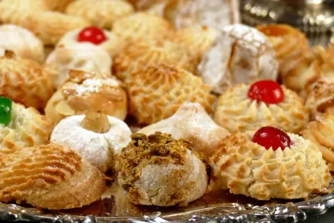 Vassoio pieno di dolcetti invitanti, tra cui spiccano le paste di mandorla decorate con ciliegie candite e granella di pistacchio.