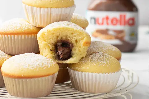 Muffin soffici con cuore di Nutella, perfetti per chi ama le ricette dolci. Un vasetto di Nutella sullo sfondo.