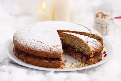 Torta di grano saraceno trentino con marmellata, spolverata di zucchero a velo, su un letto di neve e candele accese.