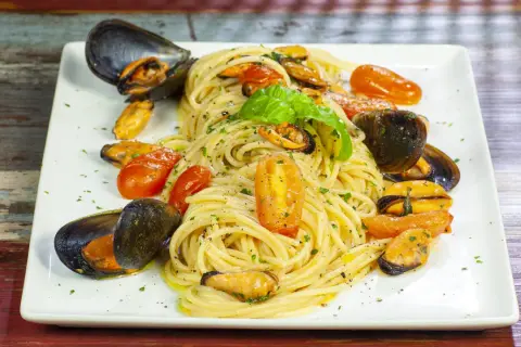 Un invitante piatto di spaghetti con le cozze e pomodorini, guarnito con basilico fresco.