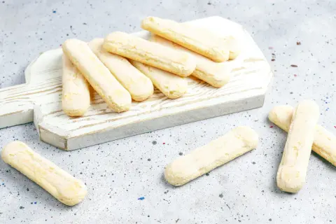 Savoiardi pronti per la ricetta del tiramisù, disposti su un tagliere bianco.