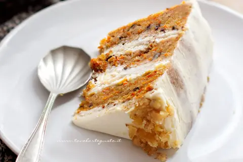 Una fetta di torta di carote, soffice e ricca, con glassa bianca e noci tritate.