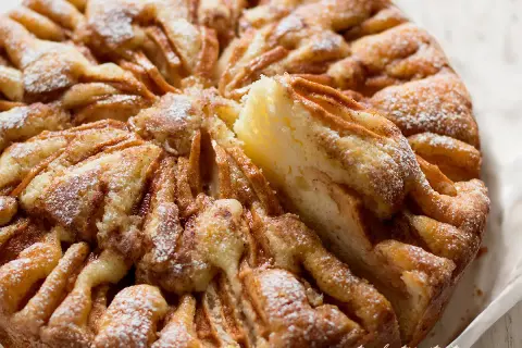 Una fetta di torta di mele morbidissima, cosparsa di zucchero a velo, con un aspetto invitante e casalingo.