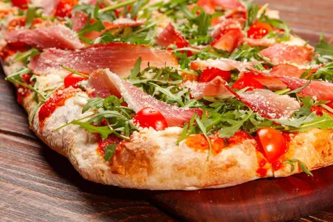 Pizza bianca con prosciutto crudo, pomodorini e rucola, cosparsa di parmigiano. Un'esplosione di sapori su un impasto soffice.