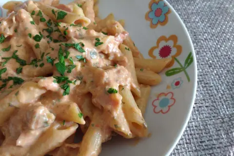 Penne al baffo cremose e gustose, condite con un sugo rosato e prezzemolo fresco, servite su un piatto decorato con fiori colorati.