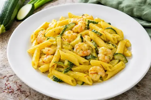 Piatto di pasta penne con zucchine e gamberetti, condito con una salsa cremosa e fili di zafferano.