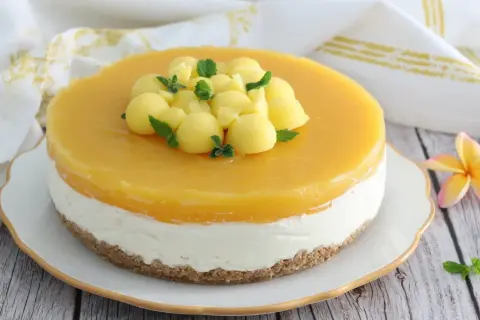 Cheesecake al mango con palline di frutta e menta fresca, su una base croccante. Un dolce estivo invitante.