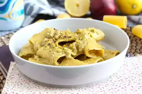 Piatto di pasta tonno e limone, condita con una crema verde e pistacchi tritati, servita in una ciotola bianca.
