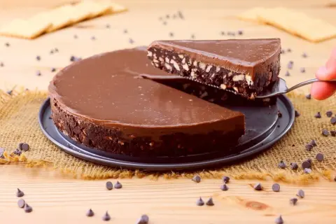 Una fetta di golosa torta fredda al cioccolato, con biscotti sbriciolati e una lucida glassa, viene sollevata da una paletta.