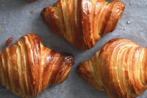 Cornetti dorati e sfogliati, perfetti per la ricetta cornetti fatti in casa. Si intravedono gocce d'acqua sulla carta da forno.