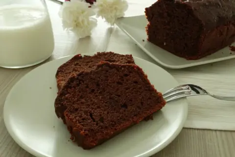 Fette di plumcake al cioccolato su un piatto, con una forchetta e un bicchiere di latte sullo sfondo.