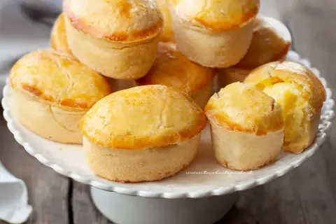 Un mucchio di pasticciotti pugliesi dorati e invitanti su un alzatina bianca.