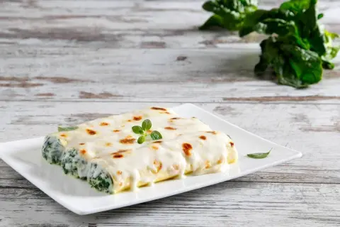 Cannelloni ricotta e spinaci gratinati, serviti su un piatto bianco con una guarnizione di origano fresco.