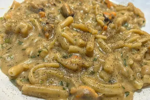 Un piatto cremoso di pasta fagioli e cozze, condito con prezzemolo fresco e pepe nero macinato.