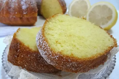 Fette di ciambellone al limone spolverate di zucchero a velo, con limoni freschi sullo sfondo.