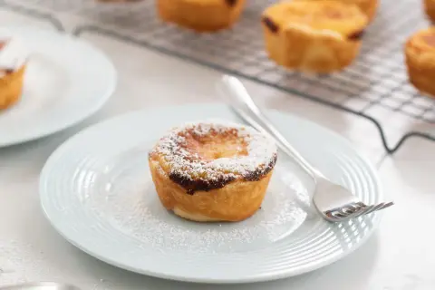 Un delizioso pastel de nata, cosparso di zucchero a velo, su un piatto azzurro con una forchetta.