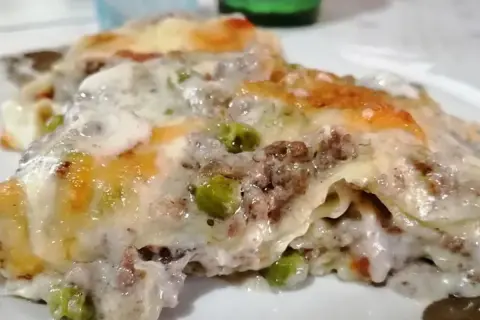 Porzione di lasagna bianca con ragù, piselli e besciamella filante, gratinata al forno.