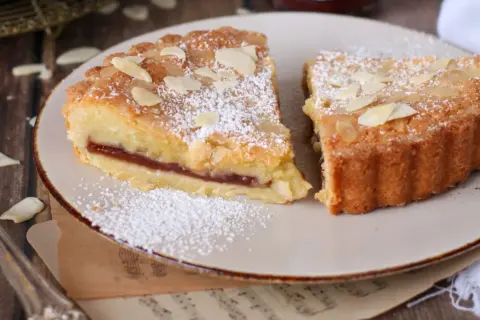 Fette di crostata frangipane con marmellata e mandorle, spolverate di zucchero a velo.