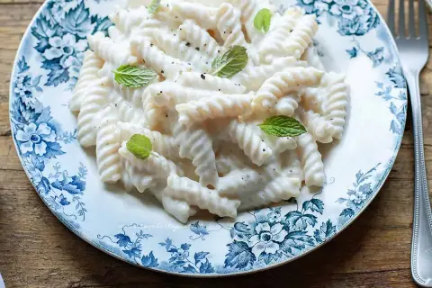 Fusilli cremosi conditi con una salsa vellutata alla ricotta, guarniti con foglie di menta fresca su un piatto decorato.
