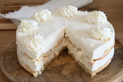 Torta soffice con strati di pan di Spagna e crema alla ricotta, ricoperta di cocco grattugiato e decorata con ciuffi di panna.