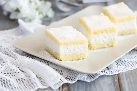 Tre soffici fette di torta Kinder Paradiso, cosparse di zucchero a velo, su un piatto bianco.