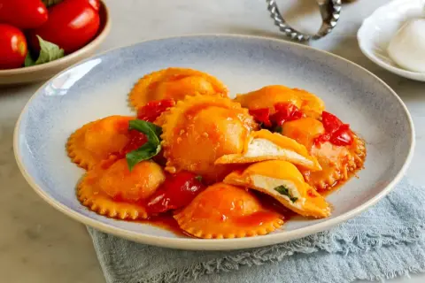 Ravioli capresi ripieni di ricotta e basilico, conditi con salsa di pomodoro fresco e guarniti con foglie di basilico.