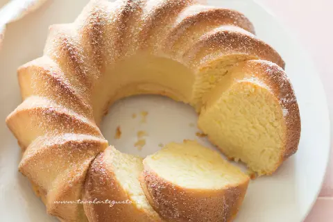 Una soffice torta di ricotta, spolverata di zucchero a velo, tagliata a fette su un piatto bianco.