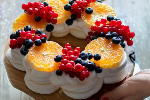 Torta pavlova a forma di corona, decorata con fette d'arancia, ribes rossi e mirtilli.