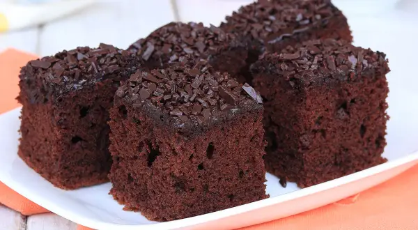 Quattro fette di torta al cioccolato morbida e umida, ricoperte di codette di cioccolato, su un piatto bianco.