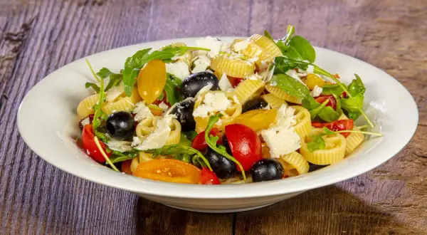 Pasta crudaiola colorata con pomodorini, olive nere, rucola e scaglie di parmigiano. Fresca e invitante.