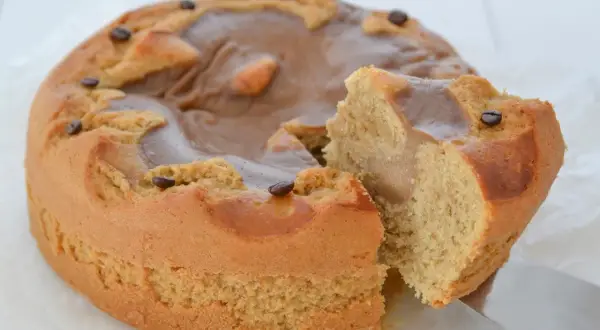Torta al caffè ricette della nonna, soffice e profumata, con glassa al caramello e chicchi di caffè. Una fetta è già stata tagliata.