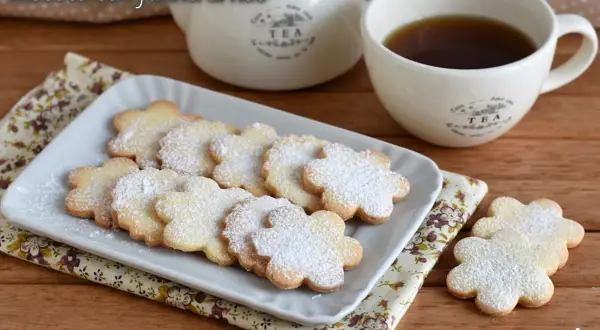 Biscotti con farina di riso a forma di fiore, spolverati di zucchero a velo, serviti con una tazza di tè.