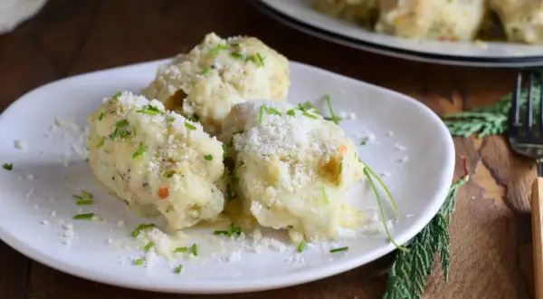 Tre gnocchi di pane soffici e dorati, cosparsi di parmigiano grattugiato e erba cipollina fresca, su un piatto bianco.