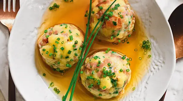 Tre canederli in brodo, guarniti con erba cipollina. Una deliziosa ricetta per un piatto tradizionale.