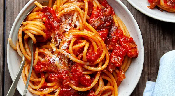Un piatto di bucatini all'amatriciana ricetta, conditi con sugo rosso e guanciale croccante, spolverati di pecorino.