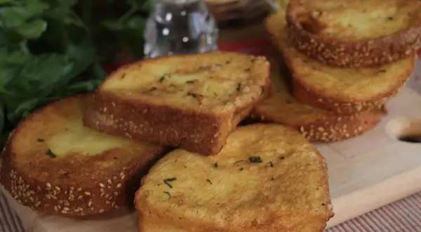 Fette dorate di pane fritto, cosparse di semi di sesamo e erbe aromatiche, pronte per essere gustate.