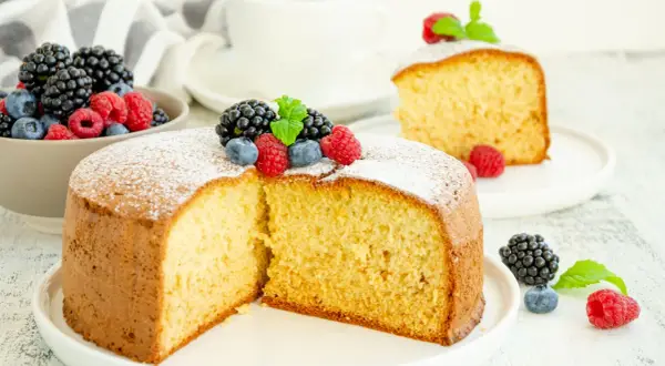 Torta soffice allo yogurt greco, decorata con frutti di bosco freschi e una spolverata di zucchero a velo.