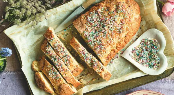 Ciambella romagnola, soffice e profumata, decorata con zuccherini colorati. Una fetta invitante, pronta per essere gustata.
