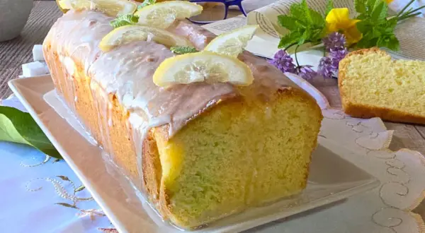 Un delizioso plumcake al limone glassato, decorato con fette di limone e menta, pronto per essere gustato.